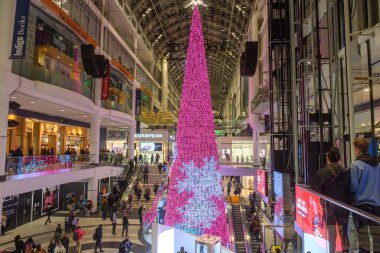 Toronto, ON, Kanada - 24 Aralık 2025: CF Eaton Merkezi 'nin iç mimarisi, üzerinde bir yıldız bulunan, üzerinde parlak pembe bir Noel ağacı bulunan, müşteriler çeşitli katlarda dolaşırken,
