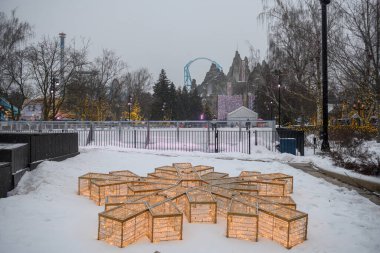 Toronto, ON, Kanada - 31 Aralık 2025: Altın ışıklarla aydınlatılmış kar tanesi şekilli dekorasyon. Arkaplanda buz pateni pisti ve Kanada Kış Festivali 'nde Wonder Mountain gösteriliyor.