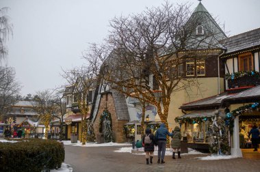 Toronto, ON, Kanada - 31 Aralık 2025: Kış Festivali 'nin tadını çıkaran insanlar, Avrupa tarzı şenlikli binaların ve sıcak sicim ışıkları ve kar yağışlarıyla süslenmiş yapraksız ağaçların yanından geçiyorlar