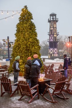 Toronto, ON, Kanada - 31 Aralık 2025: İnsanlar, Kanada Harikalar Diyarı 'ndaki kış festivalinde, karlı bir akşamda ısınmak için parlayan bir ateş çukurunun etrafında toplanıyorlar.