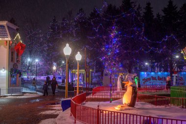 Toronto, ON, Kanada - 31 Aralık 2025: Karla kaplı parkta yürüyen insanları gösteren renkli ışık ve binalarla dolu kış festivali sahnesi