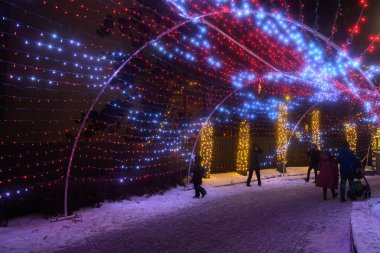 Toronto, ON, Kanada - 31 Aralık 2025: Geceleyin Kış Festivali sırasında binlerce kırmızı ve mavi telli ışığın oluşturduğu parlayan kemerin tadını çıkaran ziyaretçiler