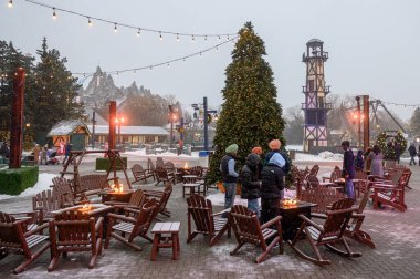 Toronto, ON, Kanada - 31 Aralık 2025: İnsanlar kendilerini bir açık hava kış festivalinde sicim ışıkları ve büyük bir Noel ağacı ile ısıtıyorlar