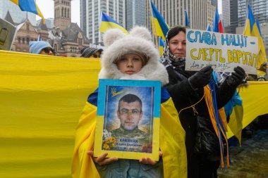 Toronto, ON, Kanada 22 Şubat 2026: Rusya 'nın Ukrayna' yı tam ölçekli işgalini protesto eden insanlar, ölen bir Ukraynalı askerin portresini tutan, anılarını onurlandıran ve barış isteyen bir çocuk.