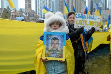 Toronto, ON, Kanada 22 Şubat 2026: Ukraynalı çocuk, işgal yıldönümü münasebetiyle düzenlenen mitingde şehit asker Vitaliy Krainiak 'ın portresini tutuyor..