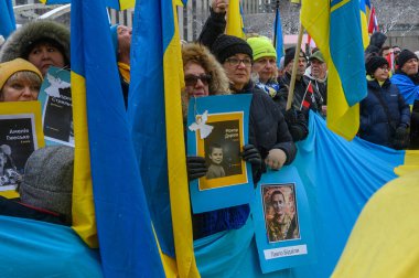 Toronto, ON, Kanada - 22 Şubat 2026: Rus işgalinin kurbanlarının anısına ellerinde Ukrayna bayrakları ve şehit düşmüş asker ve çocukların portreleri bulunan Ukrayna halkı