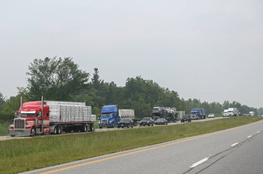 Toronto, ON, Kanada - 10 Ağustos 2025: Ağaçlarla çevrili işlek bir otoyolda kamyonlar ve diğer araçlar.