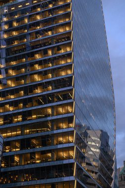 Toronto, ON, Kanada - 11 Kasım 2025: Modern bir binanın cam ön cephesi, eşsiz mimari tasarımını göstererek, şehrin alacakaranlıkta ışıklarını yansıtır.