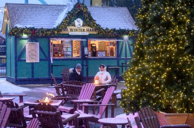 Toronto, ON, Kanada - 31 Aralık 2025: İnsanlar Kanada 'nın Harikalar Diyarı' ndaki Kış Festivali sırasında kar altında bir büfenin dışındaki ateş çukurunda ısınıyor