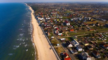 Polonya 'nın Sarbinowo kentindeki hava manzarası güneşli bir Mart gününde çekildi. Sakin Baltık Denizi, geniş kumlu plaj ve kırmızı tuğlalı kilisesi ile küçük bir kıyı kasabası huzurlu bir manzara yaratır..