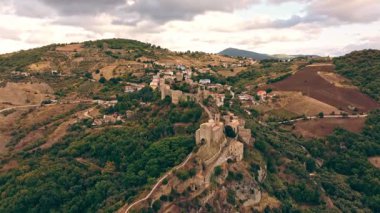 İnsansız hava aracı kayalıklardaki Roccascalegna kalesini, aşağıdaki tarihi kasabayı ve sıcak akşam ışığında manzaralı dağları yakalıyor..