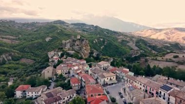 Yeşil yamaçlar, tarım alanları ve dramatik bulutlarla çevrili Roccascalegna şatosunun altın saat panoraması köyün üzerinde yükseliyor..