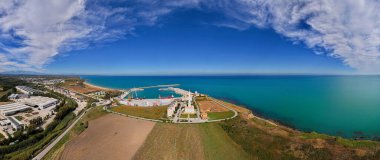 Pena Penna deniz feneri yakınlarındaki Pennaluce kilisesi yakınlarındaki Vasto limanının panoramik görüntüsü rıhtım gemileri, rüzgar türbini bıçakları, taşıma araçları ve temiz mavi kıyı suları..