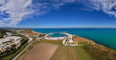 İtalya, Abruzzo 'daki Vasto limanının panoramik drone görüntüsü, liman altyapısı, kargo gemileri, turkuaz Adriyatik Denizi, çevre alanlar ve beyaz Faro di Punta Penna deniz feneri.