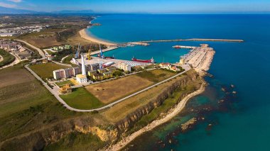 Vasto 'daki sanayi limanının gemi, turkuaz su ve çevresindeki kırsal manzaralı havadan görüntüsü..