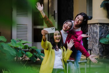 Üç neşeli genç kadın mutlu bir şekilde telefonlarıyla selfie çekiyorlar. Tatil maceralarına hazırlanıyorlar. Saf heyecan ve dostluk yayıyorlar..