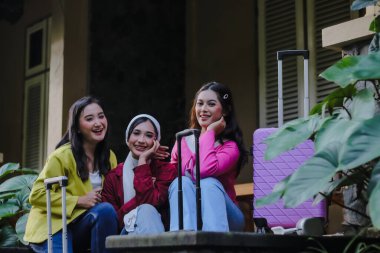 Her biri bavuluyla gülümseyen üç genç kadın yeni bir seyahat macerasına hazır. Renkli giysiler içinde, heyecan ve mutluluk yayıyorlar. Yüzleri saf dostluğu gösteriyor..