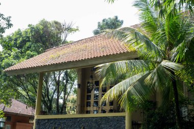 Bir villanın cephesi yemyeşil yapraklardan ortaya çıkar, kiremitli çatısı karakterle yaşlanır. Palmiye yaprakları usulca sallanıyor, gölgeler konutun duvarlarına konuyor..