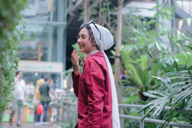 Yeşilliklerin arasında yakalanan şık bir Müslüman kadının bulaşıcı kahkahası neşeyle yankılanıyor. Kendine güveni tam ve şehir ortamında modern İslami tarzını benimsiyor..