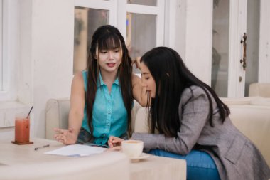 İki Asyalı iş kadını, parlak bir kafede proje belgelerini işbirliği içinde gözden geçiriyorlar. Birlikte çalışırken strateji ve yenilikçi fikirleri tartışıyorlar..