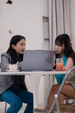 İki genç kadın kahve ve meyve suyu içerken bir kafede iş birliği yapıyor. Modern bir iş toplantısı.