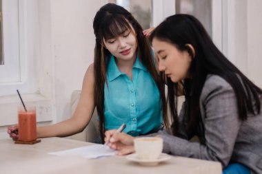İki kadın rahat bir ortamda evrakları gözden geçiriyorlar. Detaylarda işbirliği yaparlar, kahve içerler ve koşulları tartışırlar.