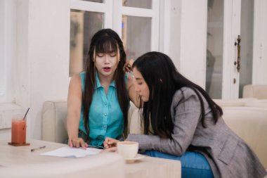 İki genç kadın işbirliği yapıyor, dikkatle kahve ile evrak işlerini gözden geçiriyorlar. Profesyonel büyüme ve tasarım stratejisi için parlak bir alanda fikirler üretmek.