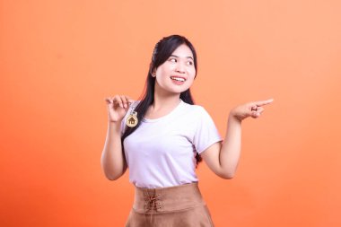 Neşeli bir kadın evin anahtarını sunar, yan tarafı gösterir, emlak fırsatlarını ve turuncu arka planda izole edilmiş yeni başlangıçları sembolize eder.