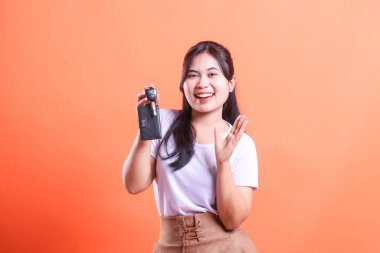 Güzel ve neşeli genç bir kadın araba anahtarlarını büyük bir gülümsemeyle tutuyor, yeni sahipliğini ve özgürlüğünü kutluyor. turuncu arkaplanda izole