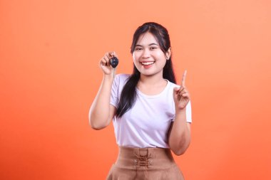 Gülümseyen bir kadın elinde bir araba anahtarı tutuyor. Yeni arabasından memnun ve turuncu arka planda izole bir şekilde yukarı bakıyor..