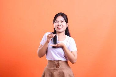 Turuncu arka planda bir bardak aktif kömür içeceği tutan ve sunan mutlu bir kadın. turuncu arkaplanda izole