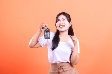 Neşeli kadın araba anahtarlarını kaldırıyor, yeni araç sahipliğini kutluyor. turuncu arkaplanda izole