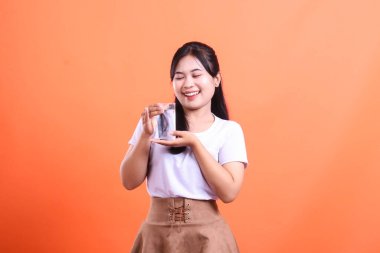 Güzel genç bir kadın bir bardak su tutarken gülümsüyor. Sağlıklı ve mutlu görünüyor. turuncu arkaplanda izole