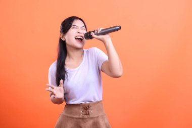 Etkileyici genç bir kadın mikrofona tutkuyla şarkı söylüyor. Yeteneğini ve enerjisini turuncu arka planda gösteriyor.