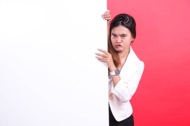 Bir kadın büyük beyaz dikdörtgen bir tabelanın arkasında kısmen görünür, yüzü tatminsizliğini ifade ediyor, kırmızı bir arkaplanda izole edilmiş.