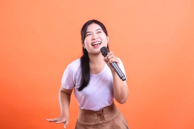 Neşeli genç bir kadın sahnede performansı sırasında mutlu ve anlamlı görünen bir mikrofonla şarkı söylüyor. turuncu arkaplanda izole