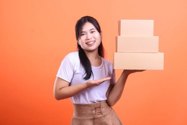 Gülümseyen bir kadın elinde üç karton kutu tutarak onları açık avucuyla sunar. turuncu arkaplanda izole