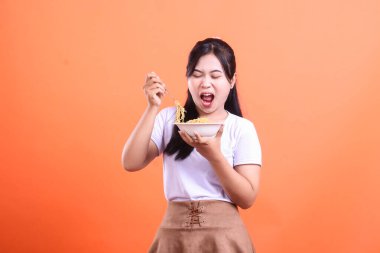 Ağzı açık bir kadın, çatalla bir porsiyon erişte yiyor, çok aç görünüyor. turuncu arkaplanda izole