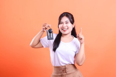 Bir numarayı gösteren arabanın anahtarlarını tutan neşeli kadın. Turuncu arka planda izole edilmiş araba sahibi kavramı.