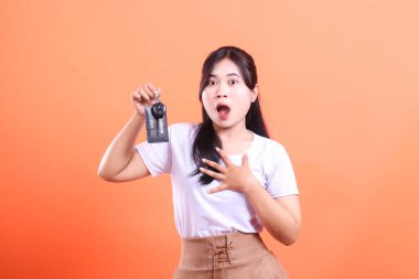 Heyecanlı bir Asyalı kadın arabanın anahtarlarını tutuyor, sürpriz ve mutluluğu ifade ediyor, muhtemelen turuncu arka planda izole edilmiş yeni bir araba aldığı için..