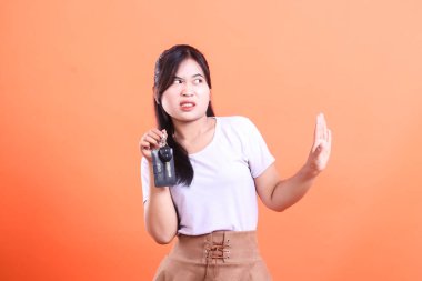 Genç bir kadın şüpheli bir yüz ifadesiyle araba anahtarlarının teklif edilmesini tasvip etmiyor. turuncu arkaplanda izole.