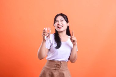 Neşeli bir kadın elinde bir bardak su tutuyor ve sağIıklı hidrasyon alışkanlıklarını ve refahı temsil ediyor. turuncu arkaplanda izole