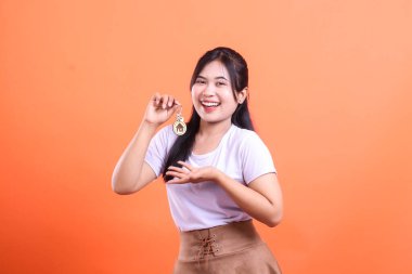 Ev anahtarlığı olan neşeli bir genç kadın ev sahibi ya da emlak alımı sergiliyor, turuncu arka planda izole edilmiş.