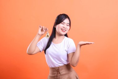 Neşeli bir kadın yeni evinin anahtarlarını ve bir sonraki hamleye hazır bir avuç içini gösteriyor. turuncu arkaplanda izole