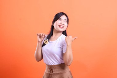 Elinde evin anahtarlarını tutarken gülümseyen ve yan tarafı gösteren genç bir kadın. turuncu arkaplanda izole