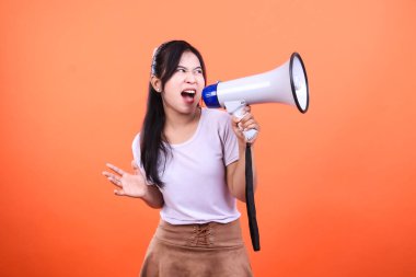 Bir kadın megafon tutuyor ve ağzı açık bağırıyor. Turuncu bir arka planda izole edilmiş..