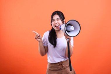 Bir kadın sol işaret parmağıyla işaret ederken sağ elinde bir megafon tutuyor. Turuncu arka planda izole edilmiş ve gülümsüyor..