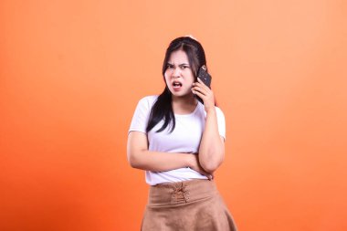 Bir kadın telefonda konuşuyor ve parlak turuncu bir arka plana karşı hoşnutsuz görünüyor..