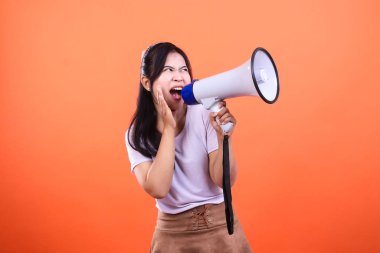 Bir kadın elinde megafonla bağırıyor, turuncu bir arka planda izole bir şekilde. Onun ağzı açık ve eli yüzüne kadar açık. O beyaz bir gömlek ve kahverengi bir etek giyiyor..