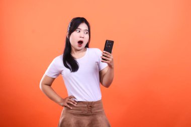 Şaşırmış bir yüz ifadesi olan bir kadın turuncu arka plandaki telefona bakıyor.